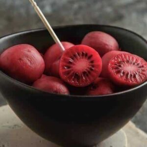 Ken's Red Hardy Kiwi Vine red skined and fleshed fruits in a dark bowl.