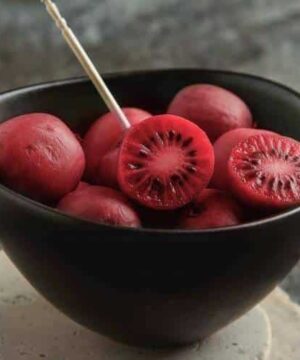 Ken's Red Hardy Kiwi Vine red skined and fleshed fruits in a dark bowl.