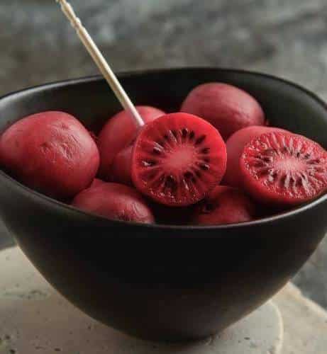 Ken's Red Hardy Kiwi Vine red skined and fleshed fruits in a dark bowl.