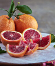 Three Blood Orange Tree fruits with orange, bumpy skin. One is cut open and has striking deep red flesh.