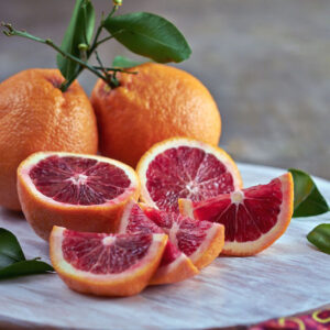 Three Blood Orange Tree fruits with orange, bumpy skin. One is cut open and has striking deep red flesh.