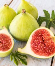 Four yellowish green Desert King Fig Tree fruits, with one fruit cut open to reveal purplish red flesh.