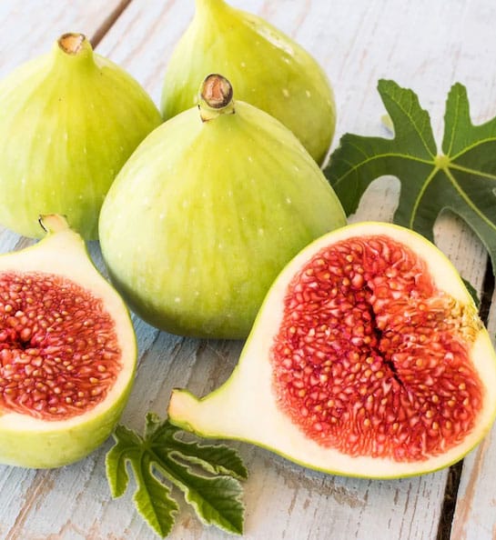 Four yellowish green Desert King Fig Tree fruits, with one fruit cut open to reveal purplish red flesh.