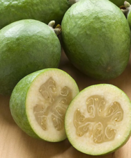 A group of Takaka Pineapple Guava plant green fruits, with one cut in half revealing a creamy centre.